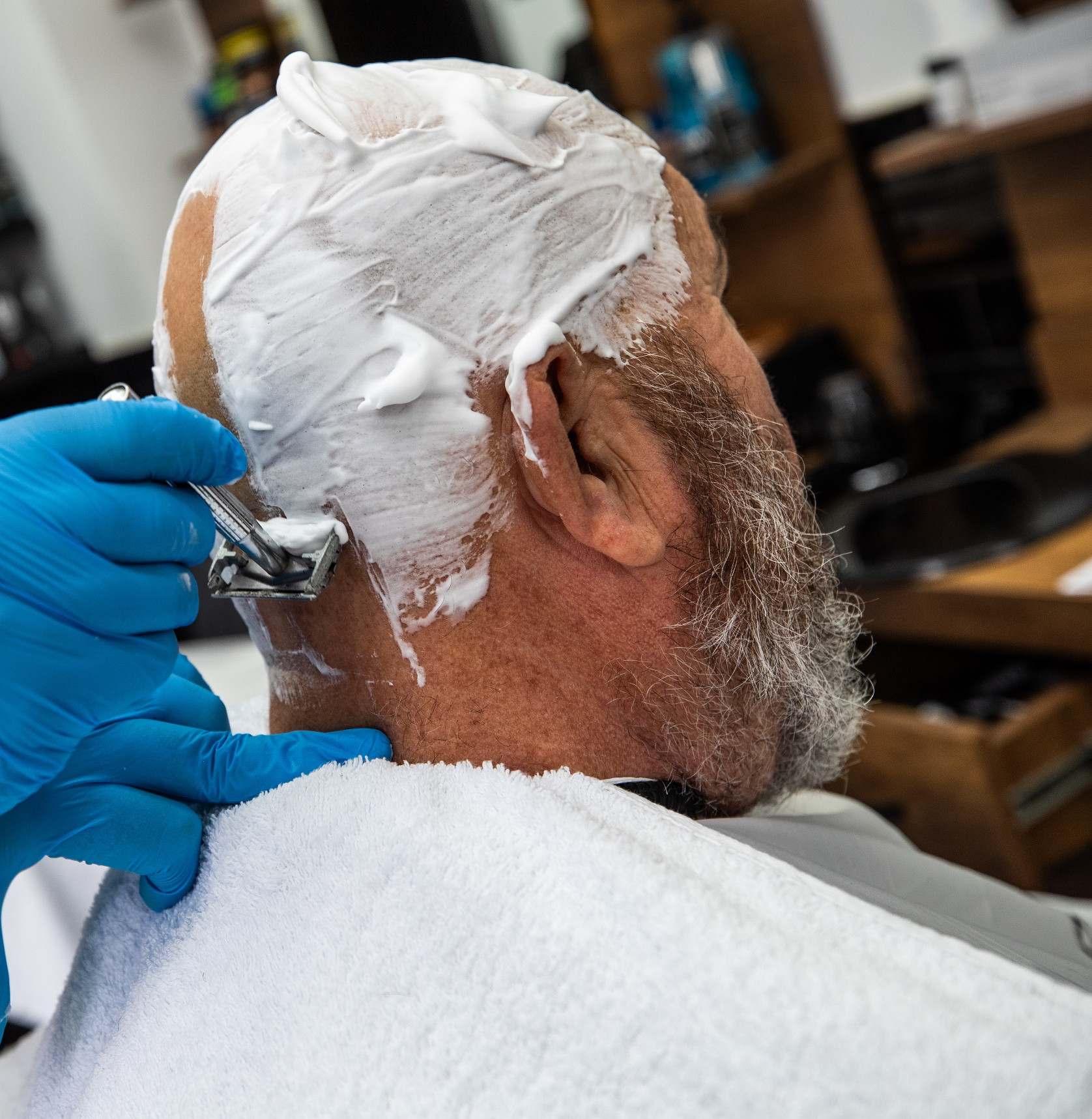 Close up of a safety razor clearing shaving foam above a client's ear